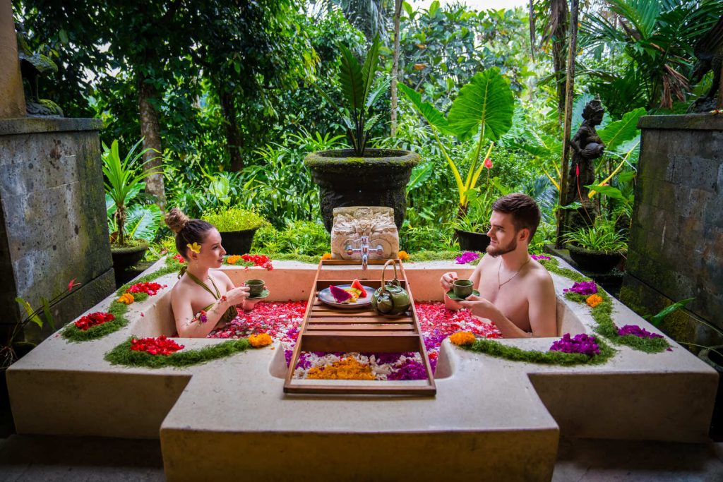 Couple enjoying a romantic Bali flower bath surrounded by tropical garden greenery, sipping tea and relaxing at Dewi Gangga Spa Ubud